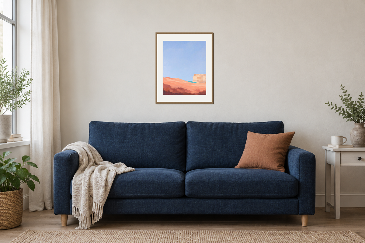Coral Dune Below Blue Sky in an oak frame above a navy sofa, with a clay cushion and oatmeal throw.