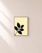 Black Leaf Sprig unframed print is shown framed for styling in a plain wall; frame not included