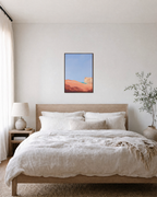 Coral Dune Below Blue Sky blue and coral abstract wall art print: unframed print is shown framed for styling in a bedroom; frame not included